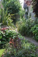 A quirky town garden in May. View from back of the garden to the house, with mixed planting of Vinca minor, Persicaria, Phormium, Yucca, and Hostas.
