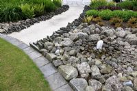 Water feature in suburban family garden for restored Art Deco house. Paths made with white sand and cement and edged with jagged slate pieces imitating the shoreline.