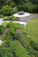 Elevated view of suburban family garden for restored Art Deco house. Paths made with white sand and cement and edged with jagged slate pieces imitating the shoreline. Curved lawn and circular decked patio area with water feature beside it.