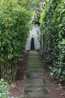 Path with focal point in suburban family garden for restored Art Deco house. Tall hedge and Bamboo