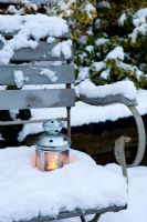 Single tea light candle lantern set in snow on garden bench seat