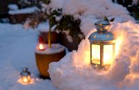 Tea light candle lanterns set in miniature snow grotto and around container grown plants