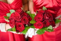 Two bouquets of Red roses held by women bridesmaids wearing red dresses