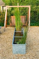 Gravel garden with metal pond and swing seat behind