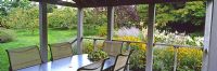 The verandah with view to orchard over large bed of flowering perennials including Rudbeckia fulgida 'Goldsturm', Perovskia atriplicifolia, Hosta sieboldiana and Cimicifuga - Rifkind Garden, Long Island, NY, USA