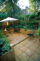 Raised beds, pot plants, paved patio, parasol and trellis in rear garden - After makeover of a Brixton garden for Channel 4 Garden Doctors