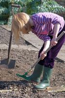 Child preparing soil with a small rake to remove stones before planting seeds in April