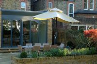 Contemporary urban garden with lighting, seating area with parasol on terrace and raised brick bed border - London