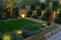 Contemporary urban garden with lighting, lawn, raised brick bed, water feature and Laurus nobilis standards - London