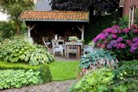 Suburban garden with wooden seats on patio. Hydrangea macrophylla, Hosta 'Frances Williams', Hosta 'Halcyon', Kirengeshoma palmata