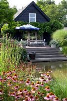 Seating area overlooking pond with perennial planting of Echinacea purpurea and Sanguisorba 
