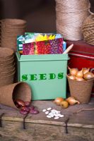 Fairtrade seed tin with seed packets, garden string, Runner bean seed 'Prizewinner stringless', Onion sets 'Turbo' and French bean seed with biodegradable planting pots on an upturned wooden crate
