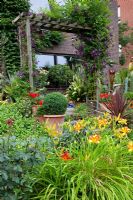 Exotic garden with plantings of Clematis, Hemerocallis 'Frans Hals' and Cordyline australis 