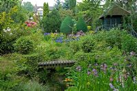 Spring garden with Iris, Primula and conifers planted around natural pond with wooden bridge and summerhouse.  Hillbark, Bardsey, Yorkshire NGS
 
