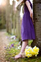 Girl with purple dress and straw hat leaning against tree with trug of daffodils