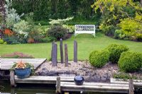 Pond area, decking with silver balls, tall grey slate plinths, mature shrubs and trees - John Massey's Garden NGS, Ashwood, West Midlands