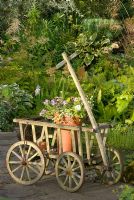 Old wooden cart as garden feature containing pot with summer bedding plants. 'Hazelwood', Jacqueline Iddon Hardy Plants, NGS garden, Lancashire 