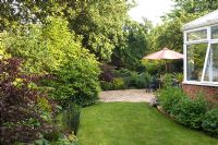 Patio in cottage garden with parasol over seating area. Windy Corner NGS, Barton, Cambs, UK 