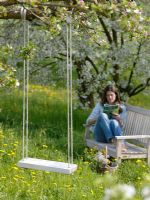 Woman relaxing on bench under an apple tree in blossom, wooden swing in foreground