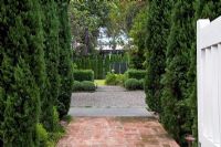 View from entrance of suburban garden with  Cupressus sempervirens - Italian Cypresses to boundary of Thuja trees at the other end. Escallonia hedges contrast with Hebe mounds across the gravelled court. Christchurch, New Zealand