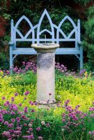 Blue gothic style wooden seat and stone sundial surrounded by Origanum vulgare 'Aureum' and Allium - Chives