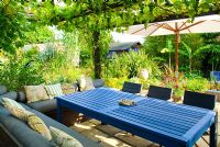 Seating under covered wooden canopy with Vitis - Grape vine. Blue table. Upholstered benches and cushions