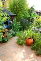 Terracotta floor tiles with glazed tile inserts. Garden shed with old flower pots and blue paintwork. Rosemary and Hedychium in containers. Musa 'Basjoo', Bamboos and Agapanthus in borders