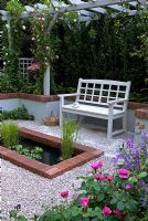 Small gravelled courtyard with wooden seat, pool and colourful borders. The 'Christian before Dior' garden - Bronze medal winner at RHS Chelsea Flower Show 2010