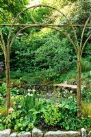 Natural arch above border of Iris Trollius, Rodgersia and Alchemilla mollis, Corylus maxima 'Purpurea', Primula chungensis. Small waterfall. The 'Music on the Moors' garden - Gold medal winner at RHS Chelsea Flower Show 2010 