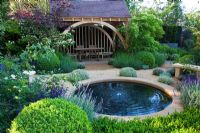 A circular pool with seating and a green oak summerhouse with planting of Buxus, Lavandula, Roses and Viburnum in The M&G Garden, Gold medal winner, RHS Chelsea Flower Show 2010 