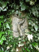 Marble wall fountain in the shape of a fish, surrounded by ivy and ferns                               