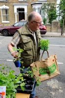 Man carrying a reusable bag, buying plants from a stall in an urban street, Hackney, London