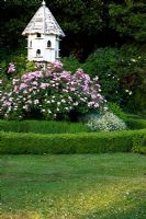 Rosa 'Rosy Cushion' around wooden dovecote - Rymans, Sussex