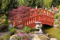 Red bridge over pool leading to the rockery in the Japanese Garden at Mount Pleasant Garden, Kelsall, Cheshire 