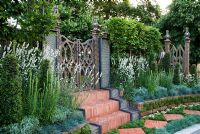 Herringbone tile steps lead up to a carved wooden gate, with rainbow effect water features, clipped pillars of Ligustrum and plants including Lavandula angustifolia 'Alba', Koeleria glauca and Armeria maritima 'Alba'. 'The Garden Lounge' - Silver Gilt Medal Winner - RHS Hampton Court Flower Show 2010 
 