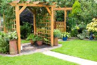 Wooden pergola with decorative path and climbers. Pots containing Ferns and Hosta and smaller arbour with gate. Meadow Ave, Southport, Lancashire. The garden opens for The National Gardens Scheme