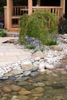 Pebble and cobble edged stream flowing past wooden circular summerhouse. The Pond Company 'Water way to go' garden.  RHS Tatton Flower Show 2010 