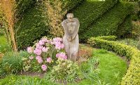 Wooden sculpture against clipped hedge, Bamboo and pink Rhododendron at Millenium Garden (NGS) Lichfield, UK, May