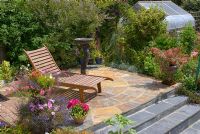 Wooden recliner on natural stone patio with colourful containers and bird bath