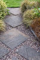 Carex, Euonymus and Uncinia rubra adjacent to gravel and paving slab path edged with slate blue stone molds. Saxon Road, Lancashire. The garden is open for The National Garden Scheme