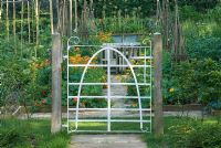 Antique hunting gate leading to the Kitchen garden. Calendula officianalis and Tropaeolum on either side of brick path with willow wigwam supports and wooden table and chairs - Heveningham, Suffolk