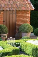 Buxus sempervirens - Box balls in terracotta pots by formal knot garden with Santolina and child's chair - Heveningham, Suffolk