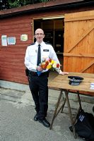 Metropolitan Police Officer with bunch of flowers outside community shed on allotment