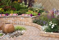 Circular cobble sett patio with central stone sphere water feature and brick walls with raised beds. Southport Flower Show 2010