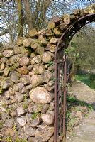 Logs piled together by the side of a metal archway to attract and provide shelter for wildlife at Summerdale House, Cumbria NGS
