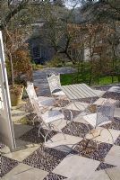 Patio with pattern made from paving slabs and embedded pebbles looking over garden in early Spring.  Summerdale House, Cumbria NGS
