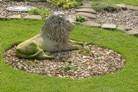 Stone lion statue in circular bed with gravel by lawn, with gravel and stone path beyond at 'Trevinia', Stubbins, Lancashire NGS