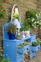 Painted dressing table with Hedera and Argyranthemum in open drawers, log pile surrounded by pots and containers with Petunia, Isotoma, Fuchsia and Verbena - 'Trevinia', Stubbins, Lancashire, NGS
