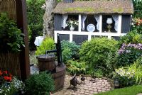 Decorative painted garden shed with thatched roof, border with Phlox, Lonicera nitida and conifers, oak barrel water feature with metal duck sculptures - Trevinia', Stubbins, Lancashire, NGS