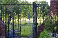 Statue of a shepherd seen through decorative gates, sited in the arboretum. Mill House, Netherbury, Dorset, UK